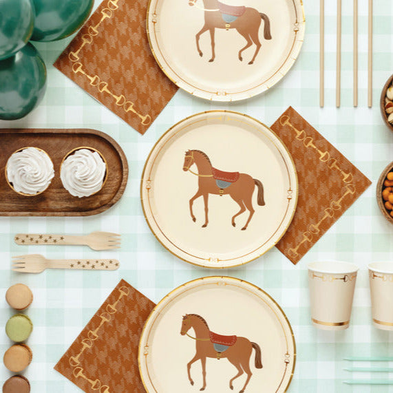 Table setting with horse-themed plates, napkins, and utensils on a light green surface.